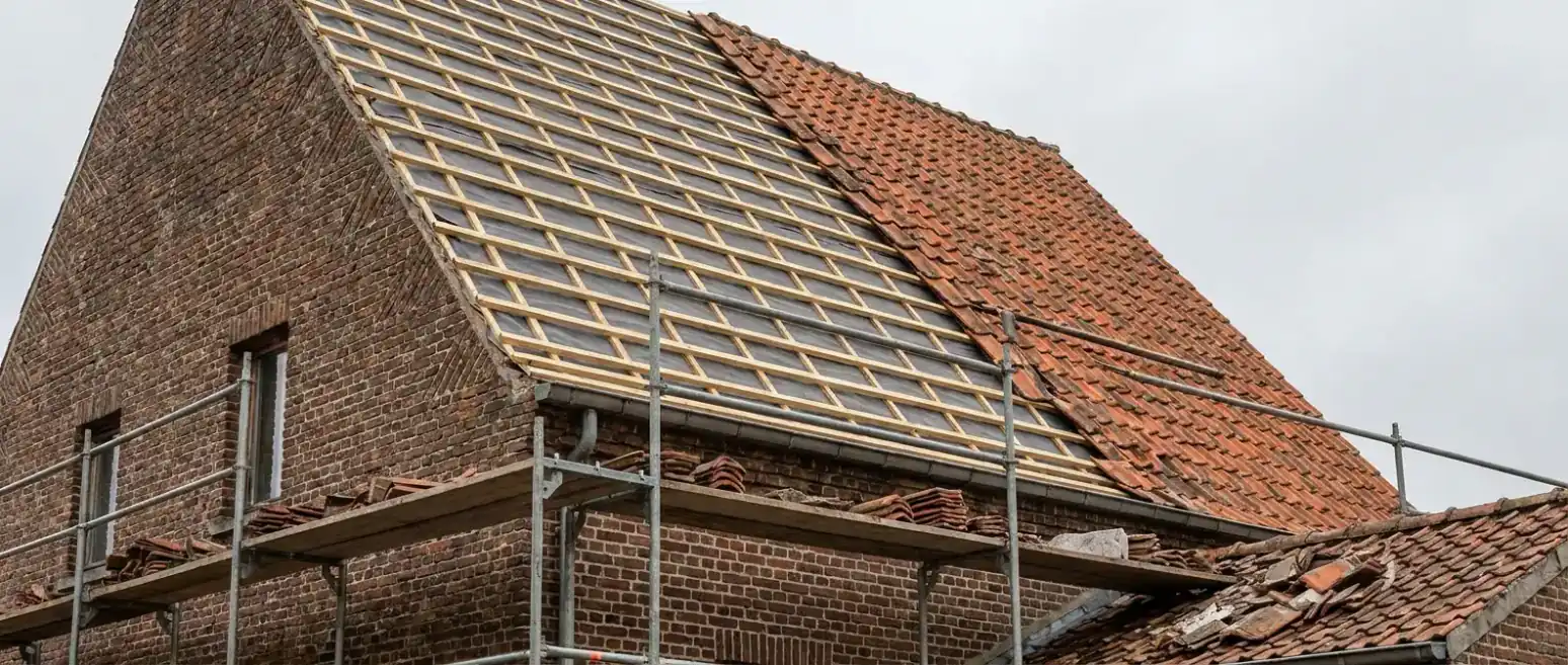 Hellend dak in renovatie waarvan de helft van de pannen is weggenomen, nieuw onderdak en tengellatten zichtbaar